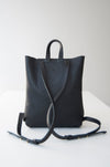 Female model wearing the Small Ray Backpack in black pebbled leather with veg tan flap