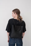 Female model wearing the Small Ray Backpack in black pebbled leather with veg tan flap